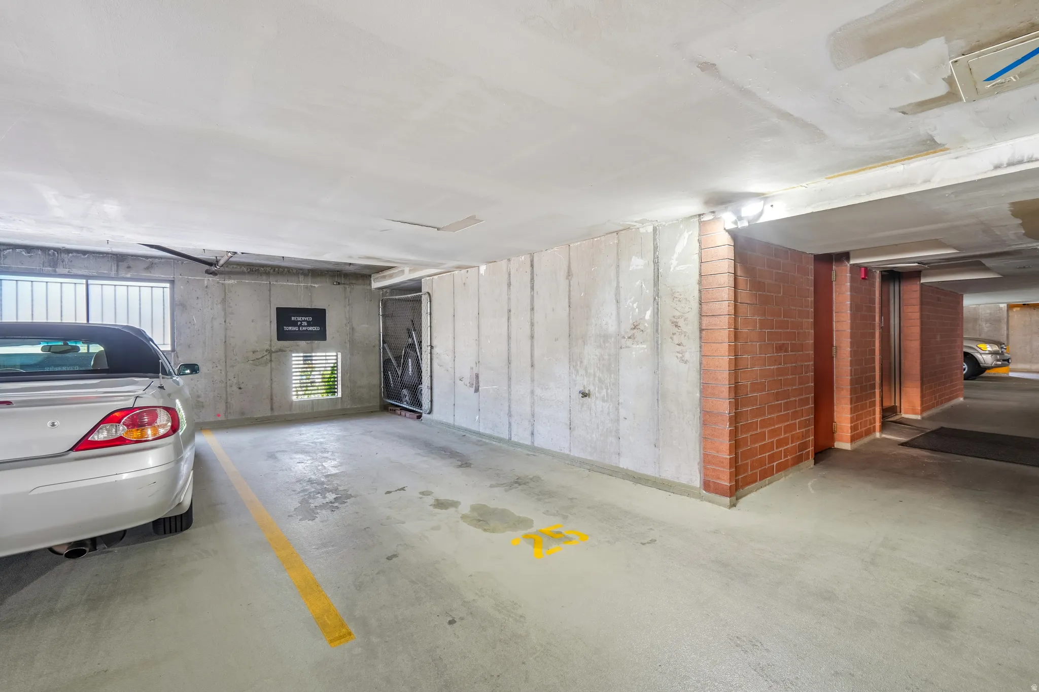Secure parking garage with concrete flooring, exposed concrete walls, brick accents, and integrated lighting