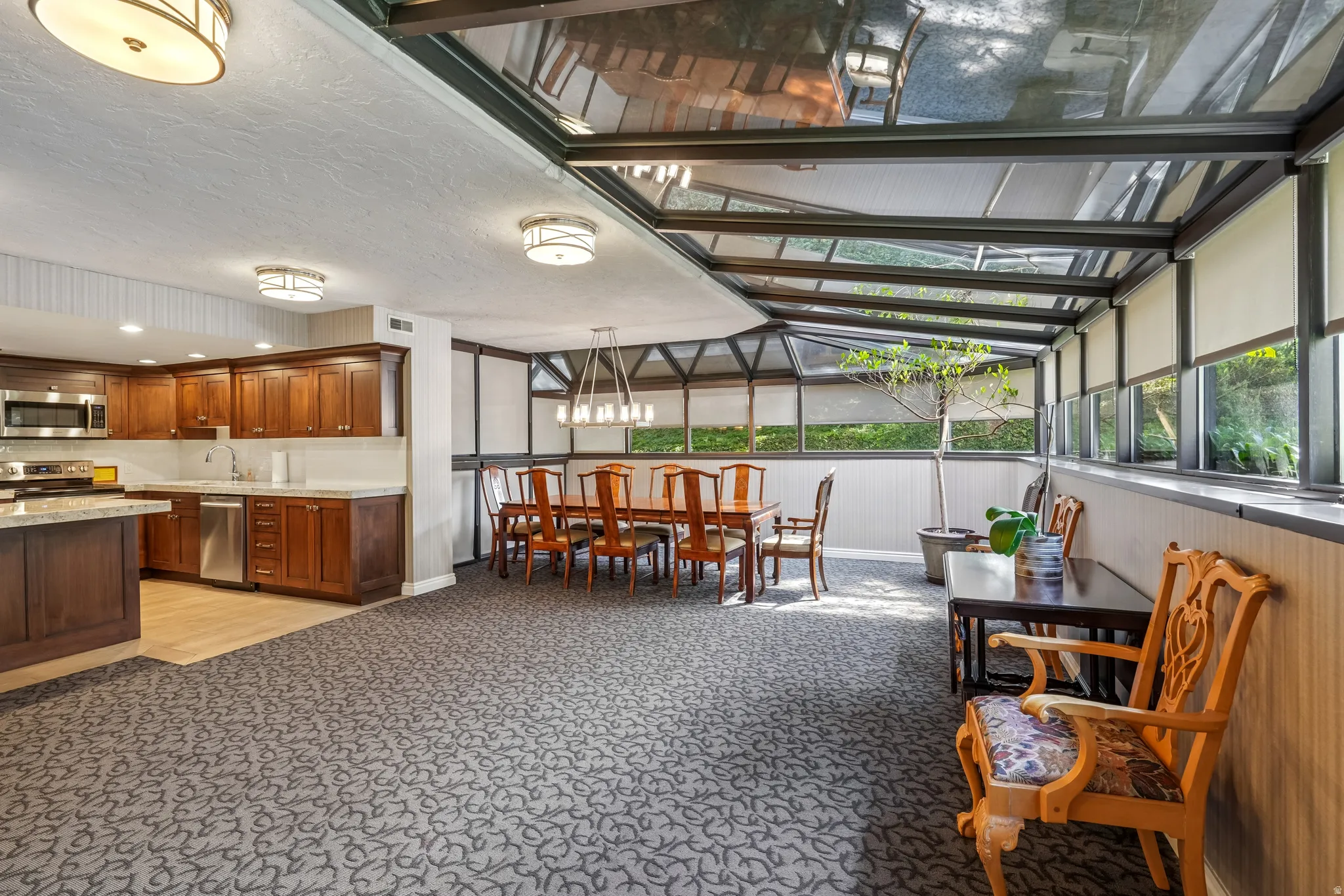 Spacious sunroom featuring a glass roof, multiple windows with roller shades, and a patterned carpet