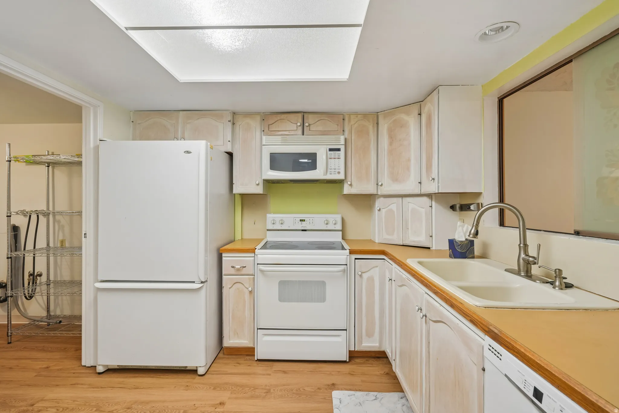 Kitchen featuring wood-finish flooring, white cabinetry, integrated white appliances, and a double basin sink with a gooseneck faucet