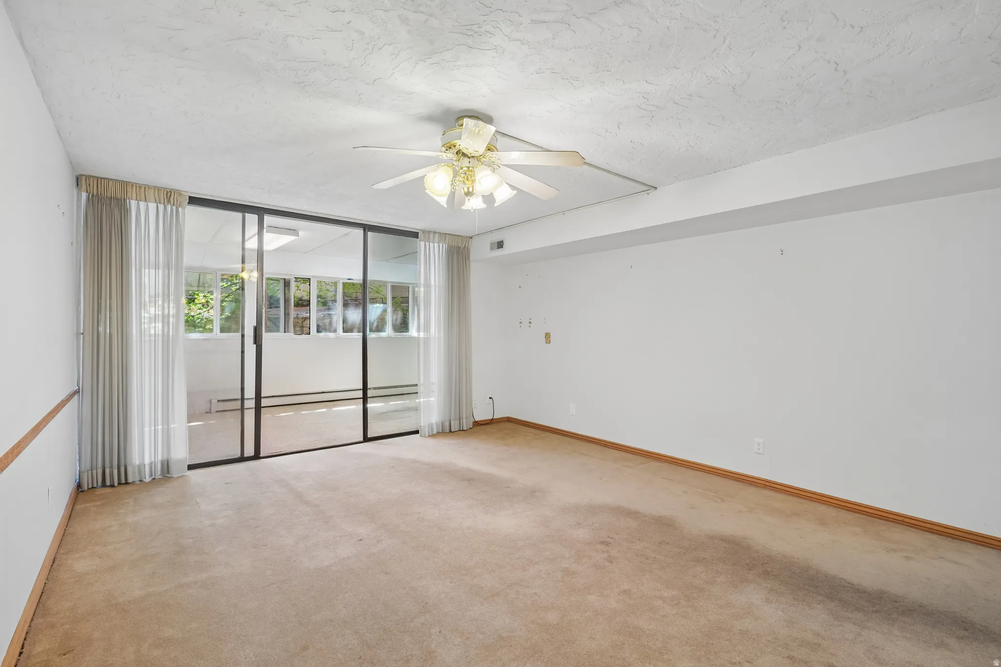 Room featuring full-wall sliding glass doors opening to a sunroom, ceiling fan, and carpeted flooring