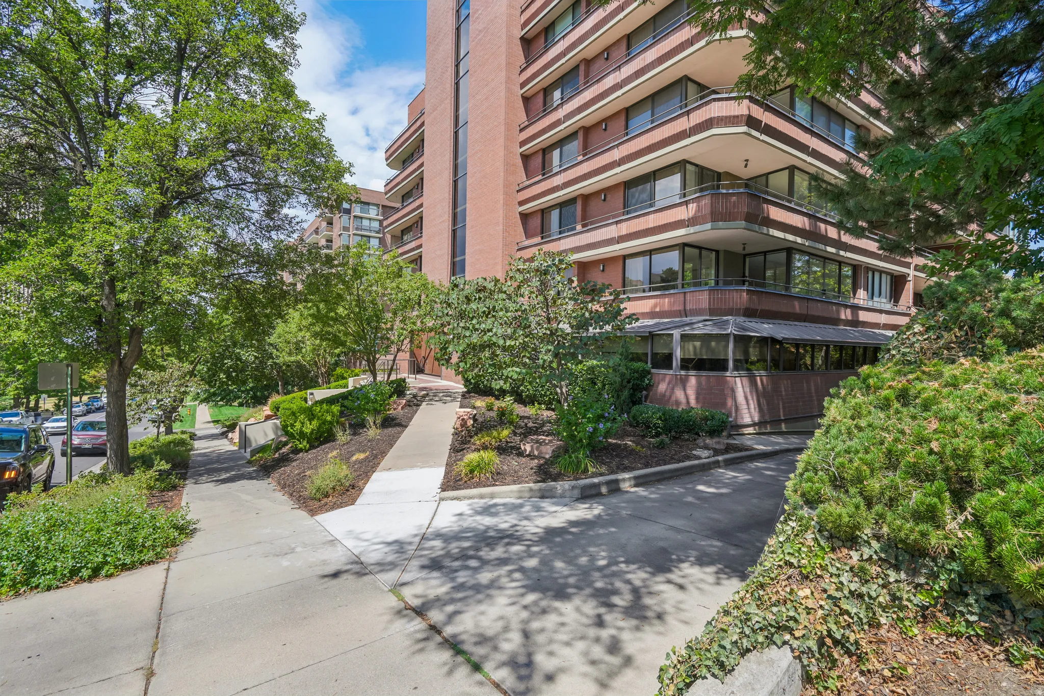 Multi-story brick facade building featuring multiple balconies with dark railings, large windows, and a prominent ground-level entrance