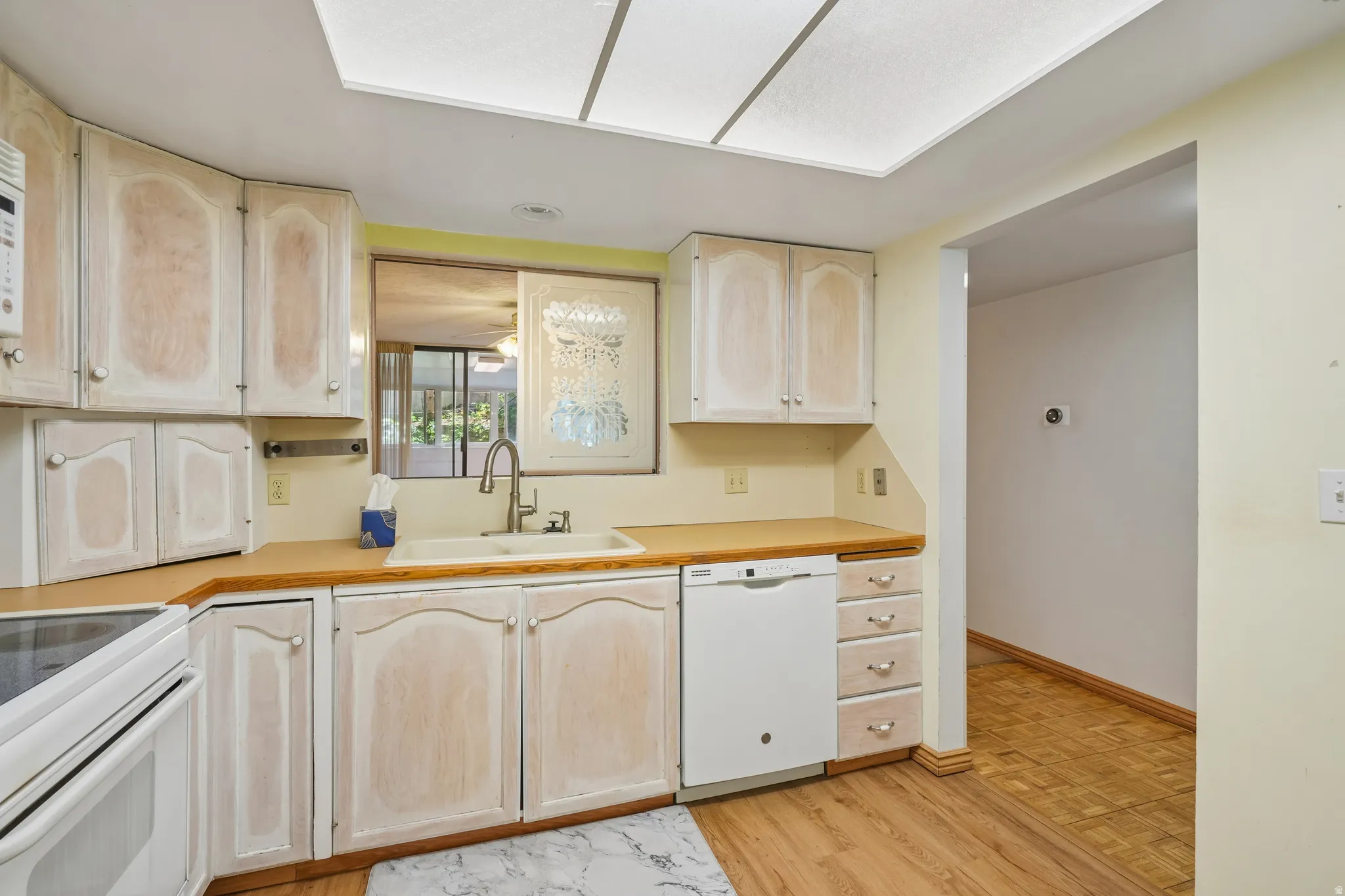 Kitchen featuring wood-finish flooring, light-toned cabinetry, a built-in dishwasher, and a pass-through window