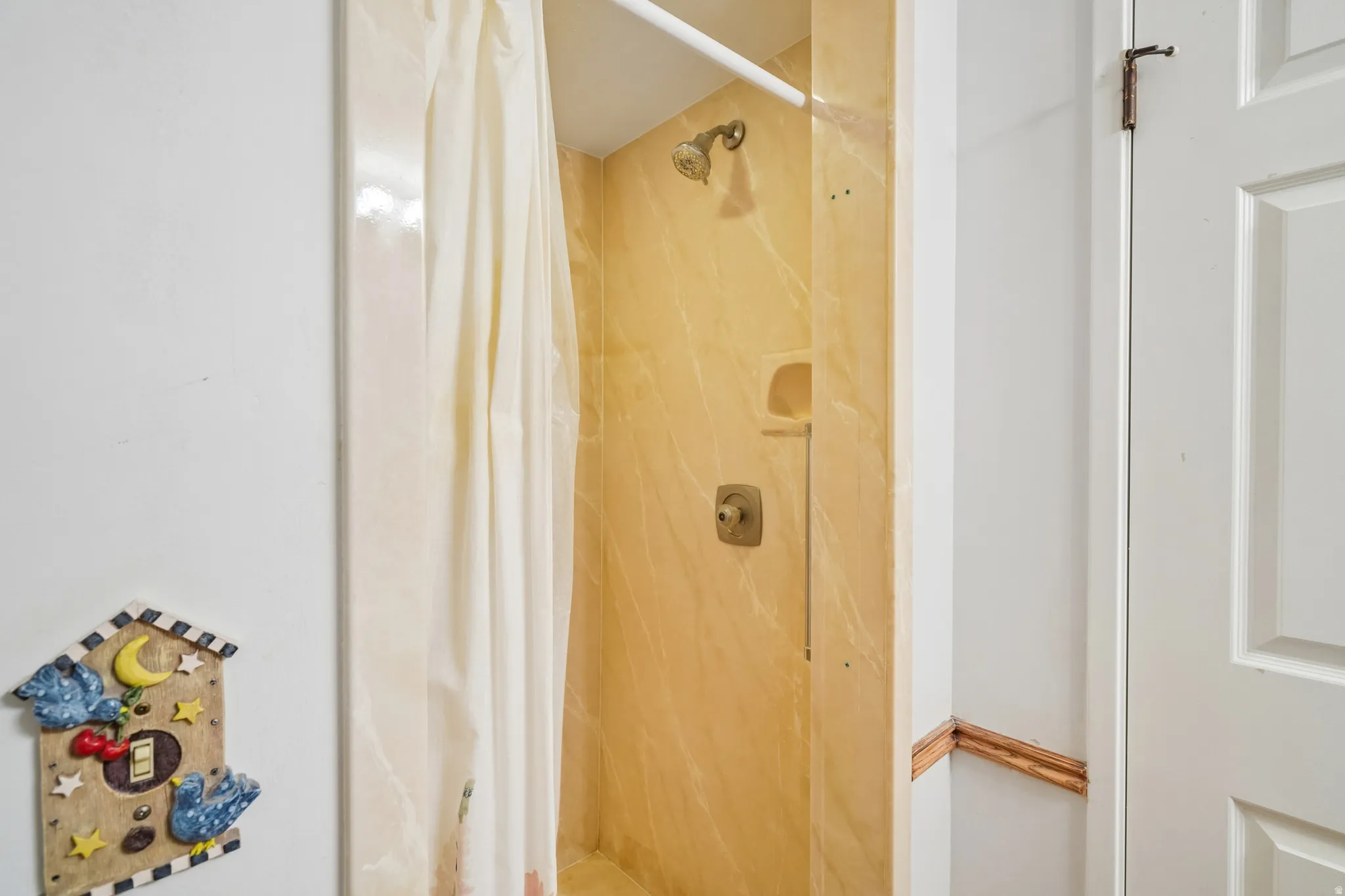 Shower stall featuring a brass-finish showerhead and controls, an integrated soap dish, and light-toned, marble-patterned wall panels