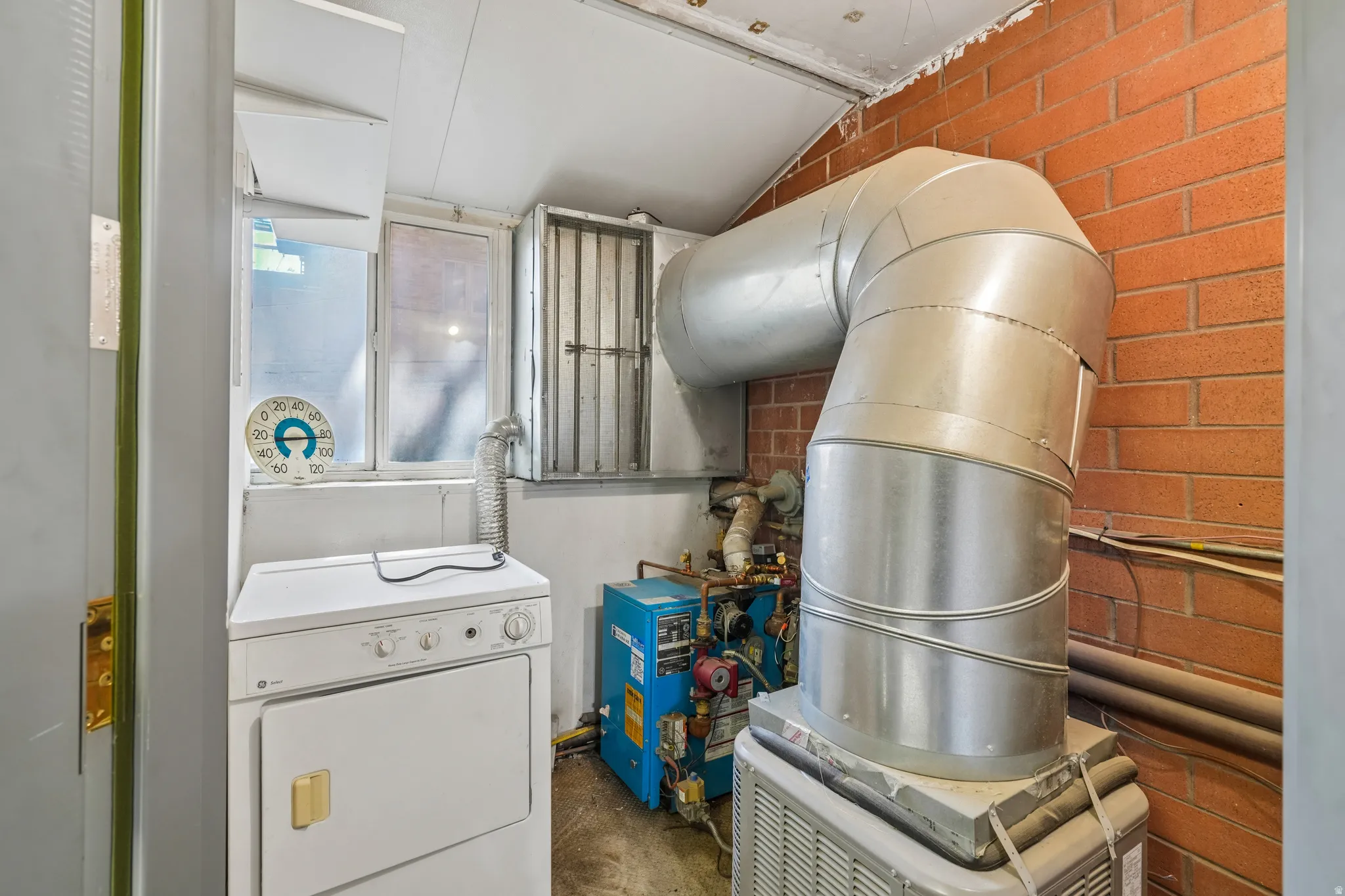Utility room featuring a window, brick wall accent, and exposed ductwork