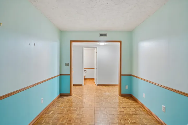 Room featuring wood-finish parquet flooring, two-tone wall paneling with natural wood trim, and a textured ceiling