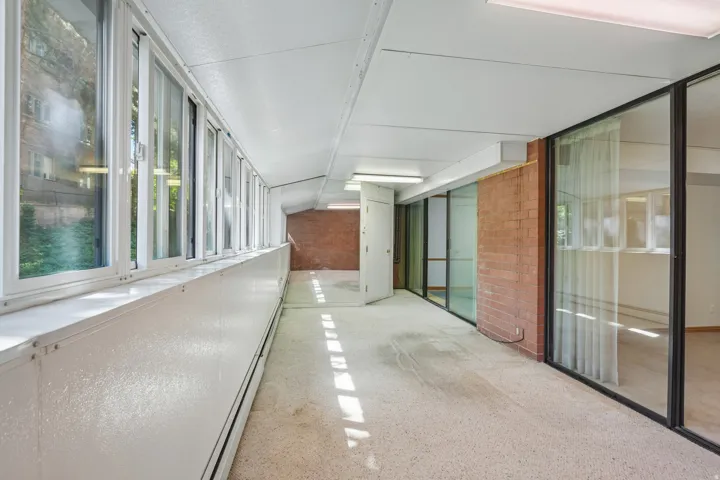 Bright corridor featuring a row of white-framed windows, a brick wall accent, and full-height glass panels