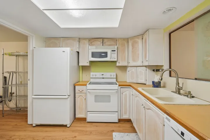 Kitchen featuring wood-finish flooring, white cabinetry, integrated white appliances, and a double basin sink with a gooseneck faucet