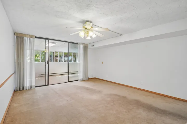 Room featuring full-wall sliding glass doors opening to a sunroom, ceiling fan, and carpeted flooring