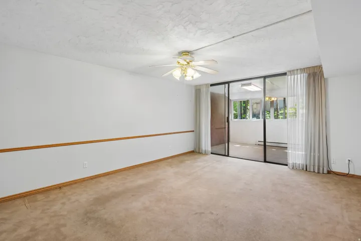 Carpeted room featuring a ceiling fan with light fixture, chair rail molding, and sliding glass doors opening to an enclosed patio