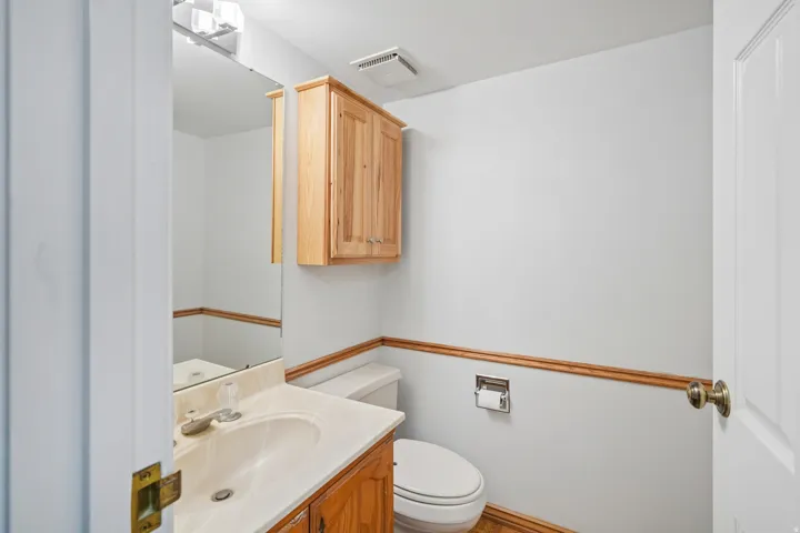 Bathroom featuring a light wood-finish vanity with an integrated sink, a matching wall-mounted cabinet, a large vanity mirror, and a classic toilet