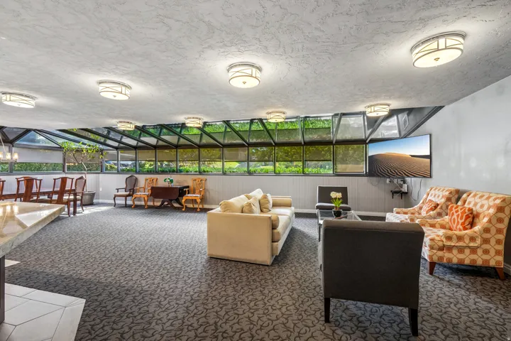 Spacious common area featuring an expansive glass ceiling, patterned carpeting, recessed lighting, and a wall-mounted display