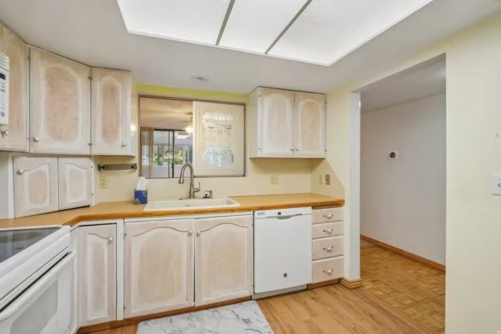 Kitchen featuring wood-finish flooring, light-toned cabinetry, a built-in dishwasher, and a pass-through window