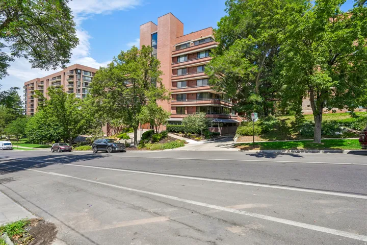 Multistory brick building exterior featuring extensive landscaping, multiple balconies, a covered entry, and a paved driveway