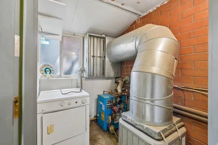 Utility room featuring a window, brick wall accent, and exposed ductwork