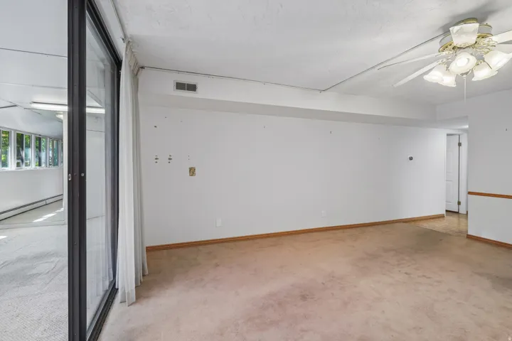 Carpeted interior space with a ceiling fan light fixture and a sliding glass door