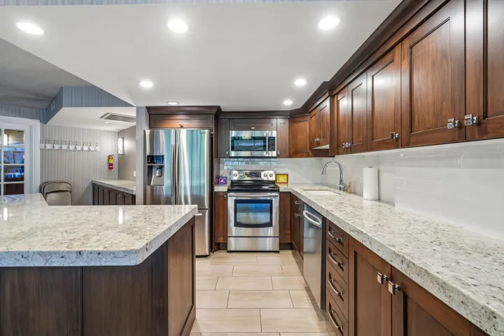 Gourmet kitchen featuring extensive light-toned granite countertops, rich wood cabinetry, stainless steel appliances, a white subway tile backsplash, and recessed lighting