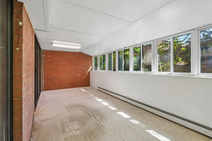 Enclosed sunroom featuring a full wall of windows, brick accent wall, white painted walls, white ceiling, and light-colored flooring
