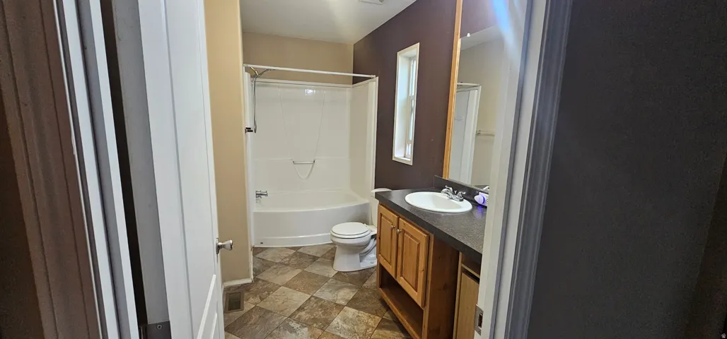 Bathroom with a white tub-shower combination, a toilet, and a vanity featuring a white sink, dark countertop, and wood-finish cabinetry