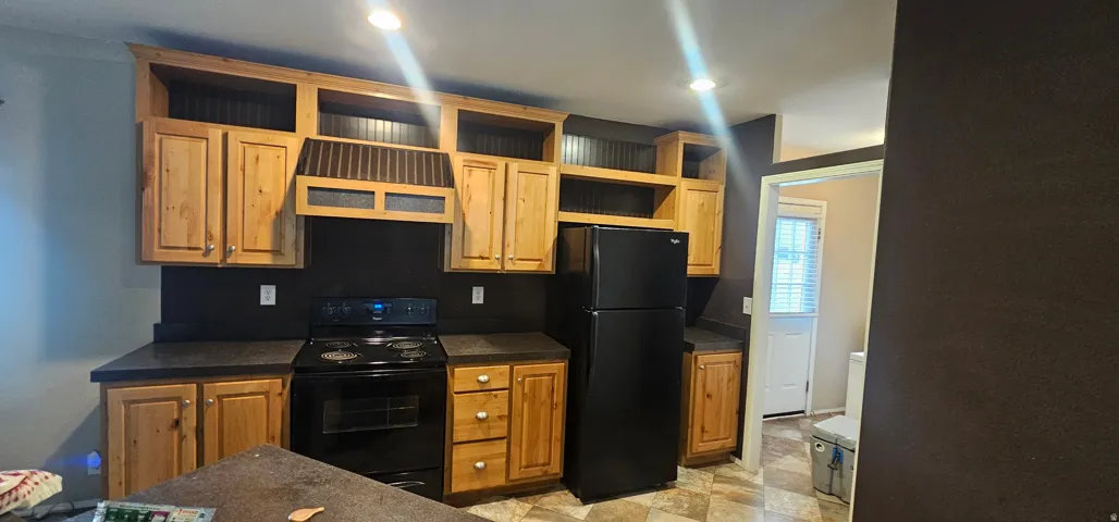 Kitchen featuring light wood cabinetry, black countertops, and a black appliance suite including a refrigerator and range