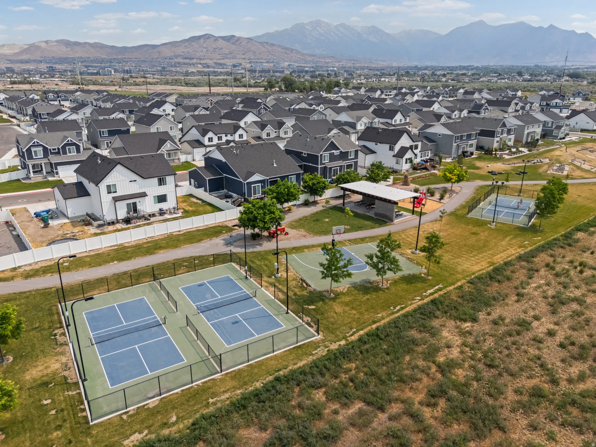 Expansive community recreational area featuring two pickleball courts, a basketball half-court, and a covered pavilion with picnic tables