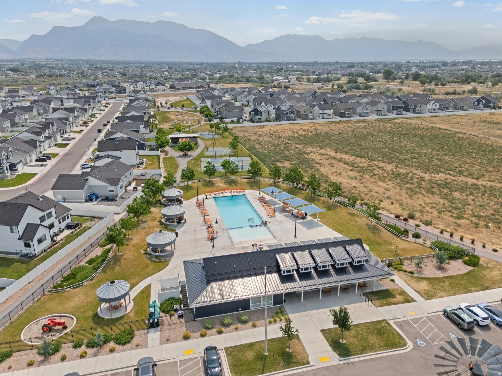 Community amenities featuring a swimming pool, clubhouse with a metal roof, multiple shade structures, and manicured green spaces