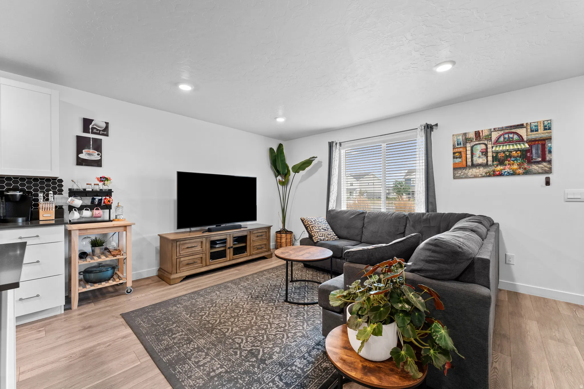 Open-concept living space with light wood-finish flooring, recessed lighting, and a window with blinds