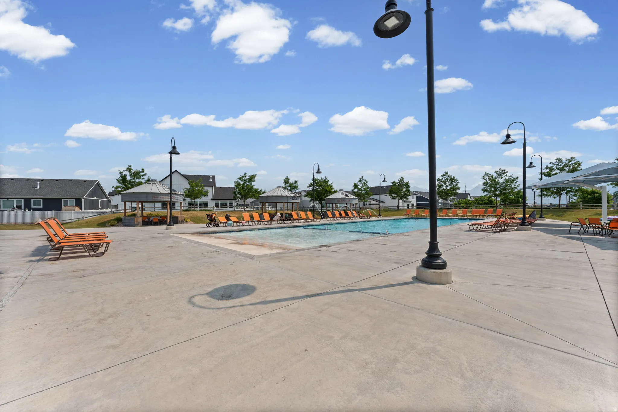 Expansive concrete pool deck featuring an in-ground swimming pool, multiple shaded cabanas, and integrated outdoor lighting