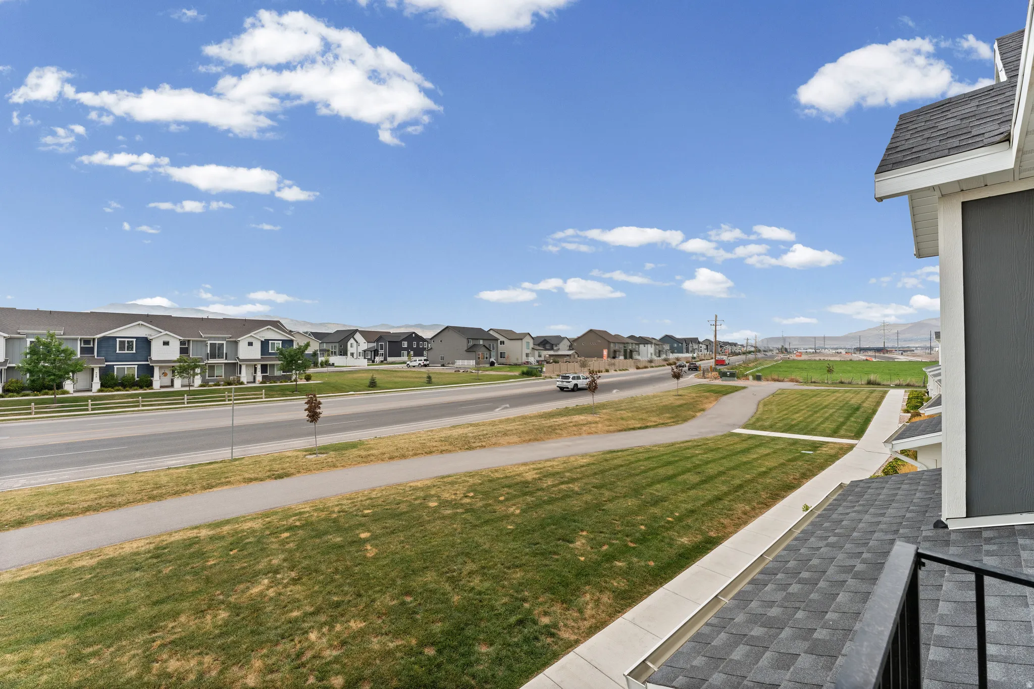 Neighborhood street featuring a sidewalk, manicured lawns, and distant mountain range