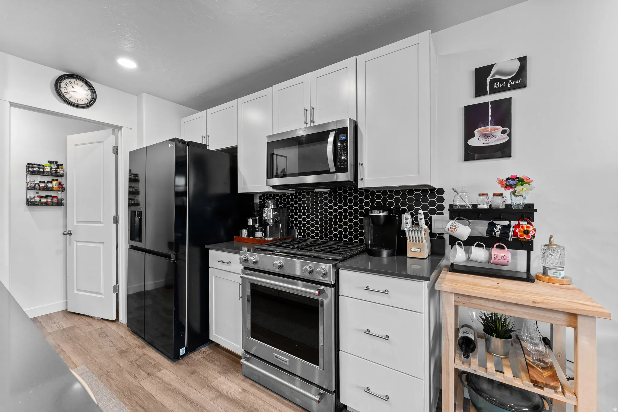 Kitchen featuring white cabinetry, dark countertops, a black hexagonal tile backsplash, stainless steel appliances, and wood-finish flooring