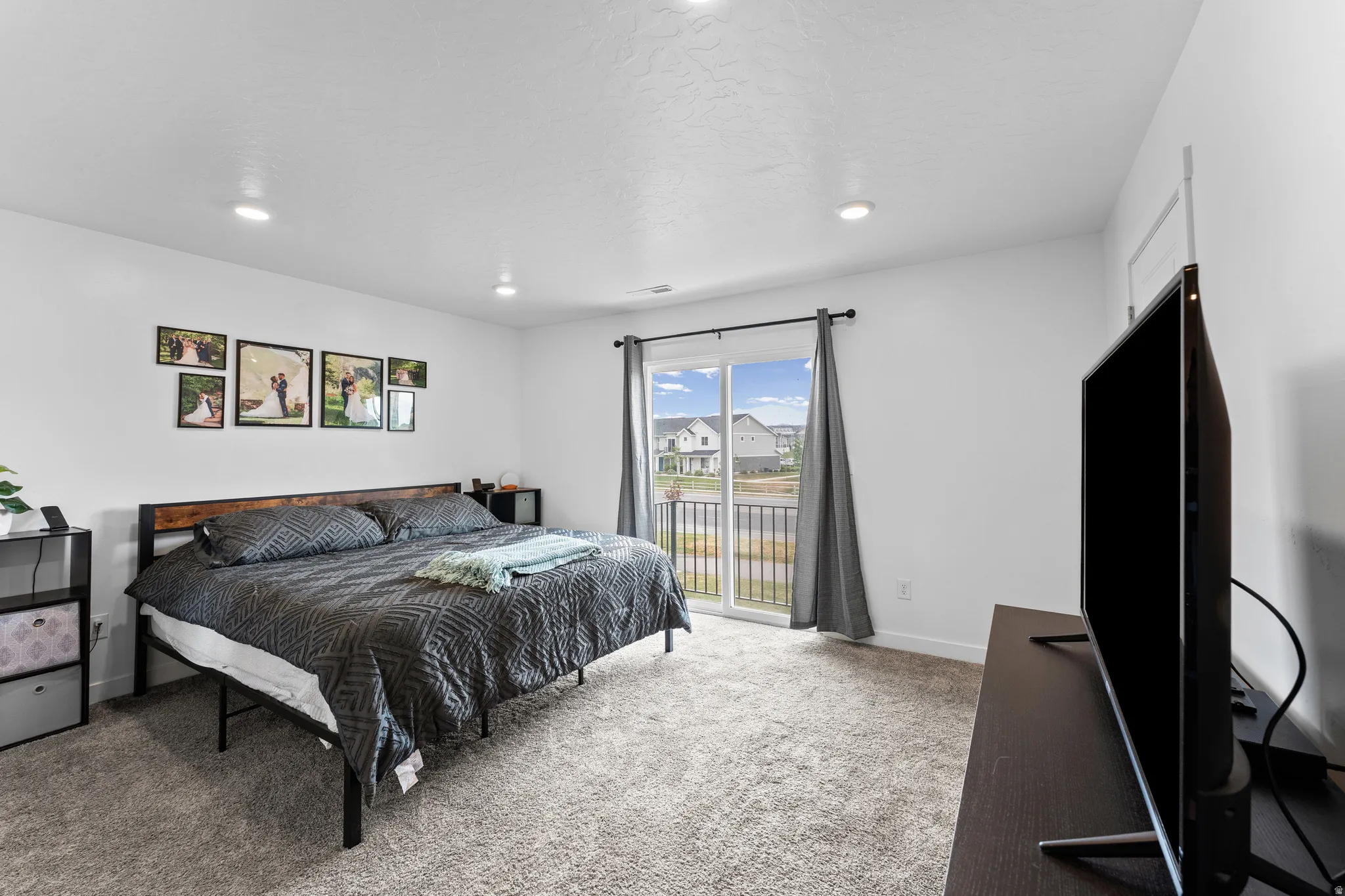 Spacious room featuring light-colored carpeting, recessed ceiling lighting, and a sliding glass door leading to a balcony with black metal railings