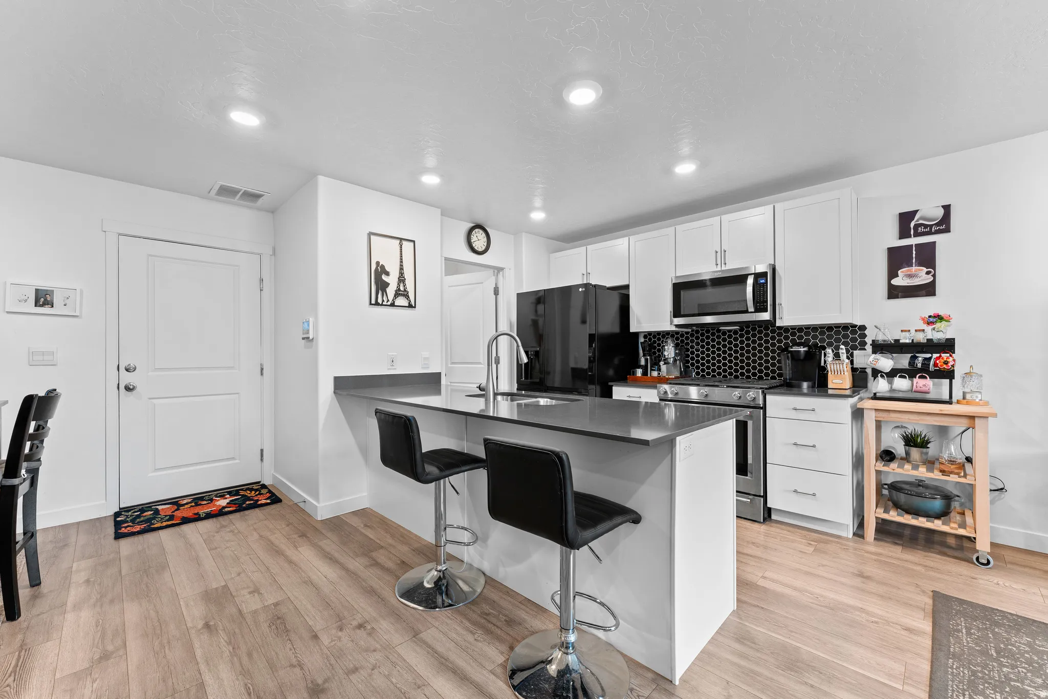 Kitchen featuring white cabinetry, a hexagonal tile backsplash, stainless steel appliances, and a central island with a sink and seating space