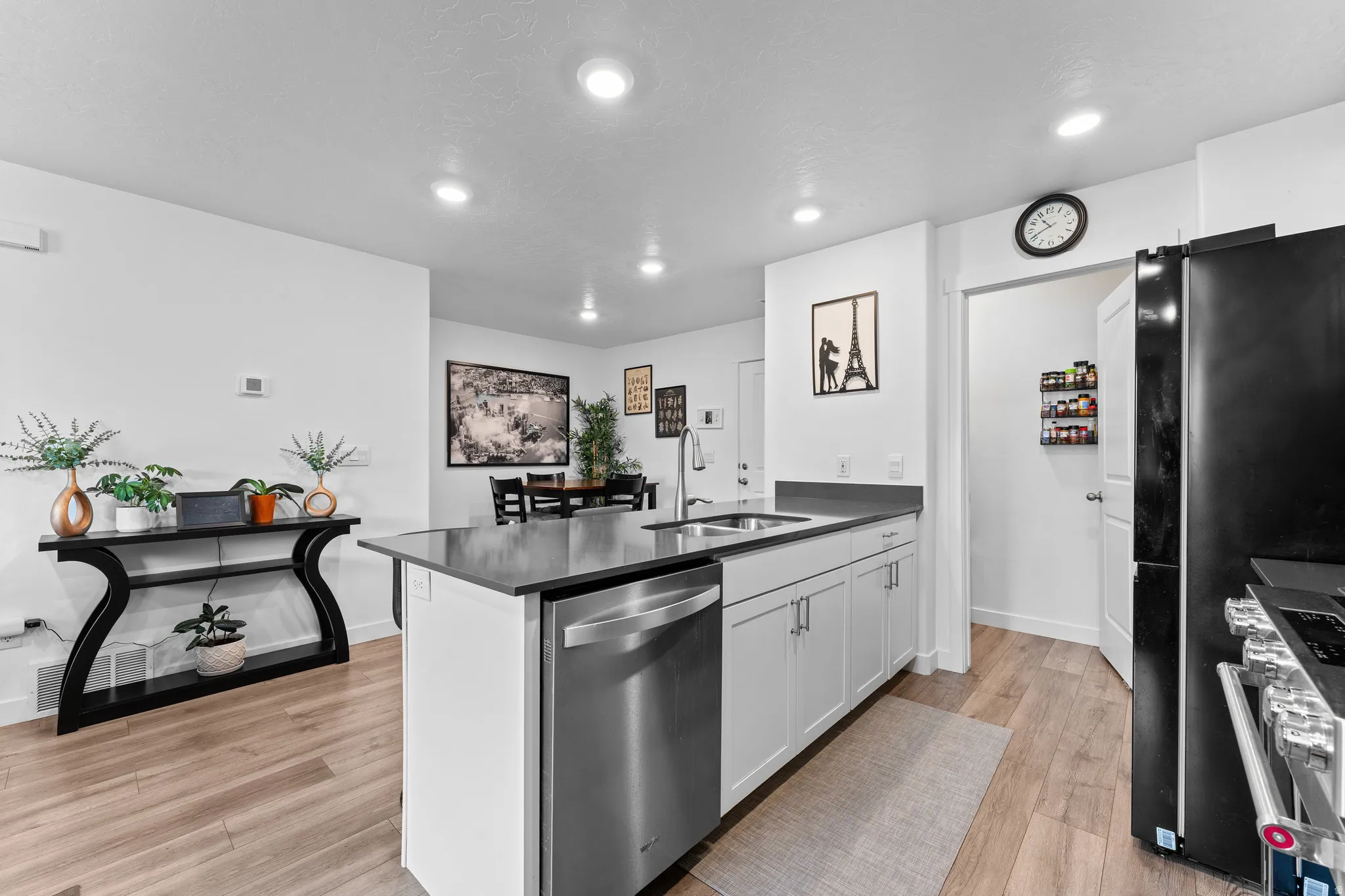 Modern kitchen with light wood-finish flooring, white cabinetry, stainless steel dishwasher, and a dark countertop island featuring an undermount sink