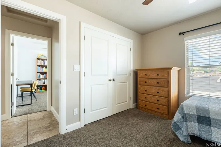 Carpeted room with a ceiling fan and a window featuring blinds