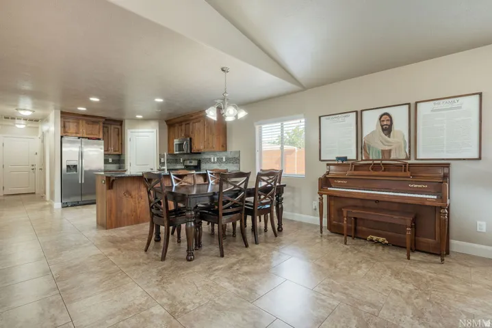 Open-concept living space featuring ceramic tile flooring, a kitchen island with seating, wood cabinetry, stainless steel appliances, and a dining area with a chandelier