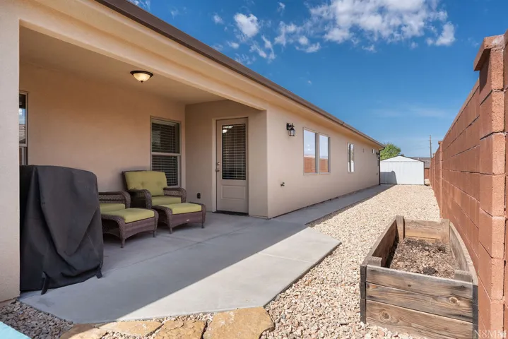 Covered patio area with concrete flooring, stucco exterior, gravel landscaping, and a detached storage shed