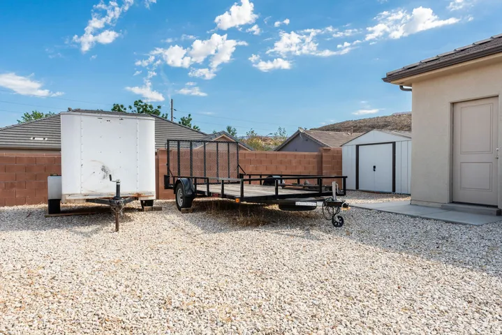 Gravel yard space featuring a detached storage shed, a tan stucco exterior, and a concrete pathway