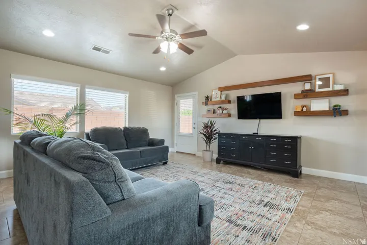Vaulted ceiling living space featuring tile flooring, multiple windows with blinds, a ceiling fan with integrated lighting, and recessed lighting