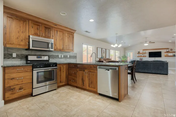 Kitchen featuring wood cabinetry, stainless steel appliances, granite countertops, and a tiled backsplash