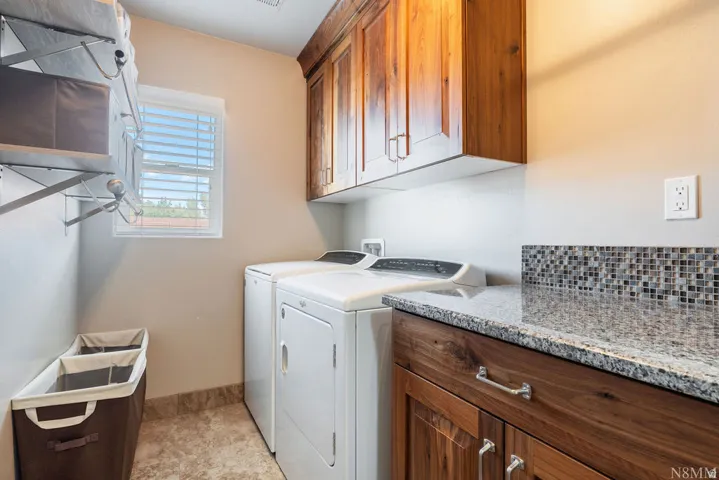 Laundry room featuring wood-finish cabinetry, granite-style countertop, and mosaic tile backsplash