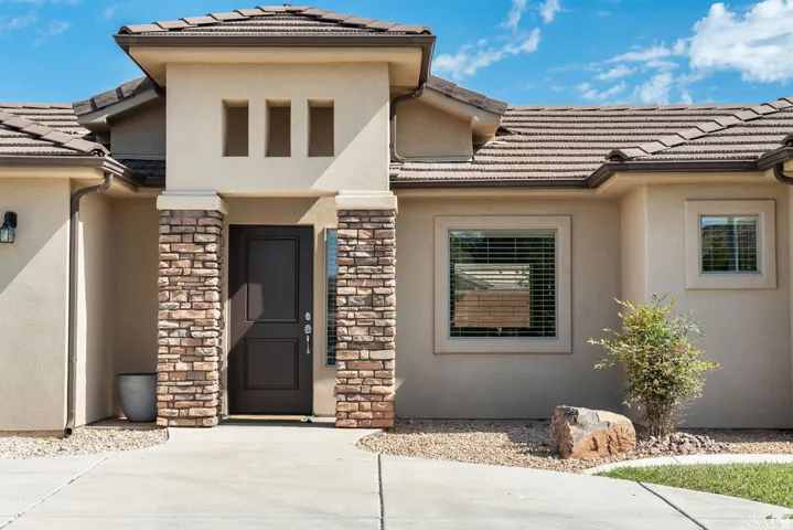 Stucco exterior featuring stacked stone columns, a dark panel door, and a tiled roof