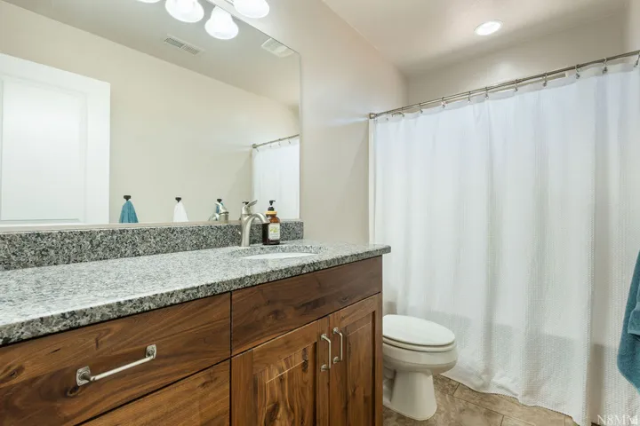 Bathroom vanity featuring a speckled countertop, wood-finish cabinetry, and a full-width mirror