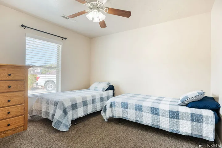 Carpeted interior space featuring neutral wall tones, a ceiling fan with integrated lighting, and a single window with horizontal blinds