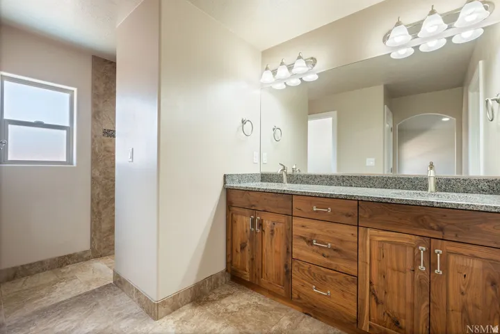 Double vanity featuring wood-finish cabinetry and a speckled stone countertop
