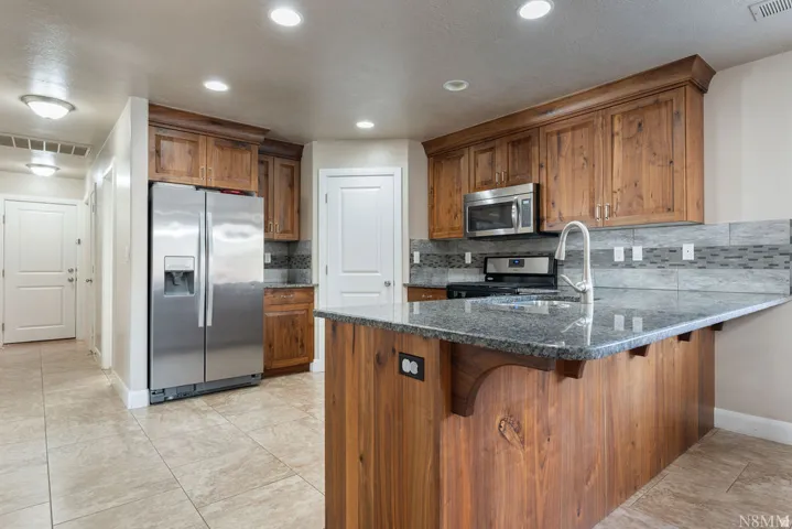 Kitchen featuring a center island with a granite countertop, wood cabinetry, stainless steel appliances, and a tiled backsplash