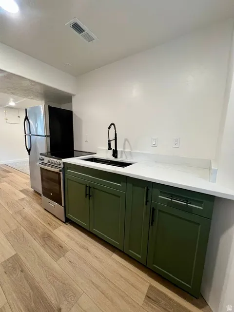 Kitchenette featuring wood-finish flooring, white countertops, and olive green cabinetry with matte black hardware