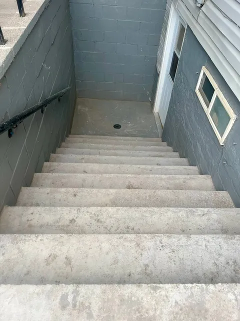 Seperate entance concrete exterior stairs with a black metal handrail leading to a painted block wall foundation