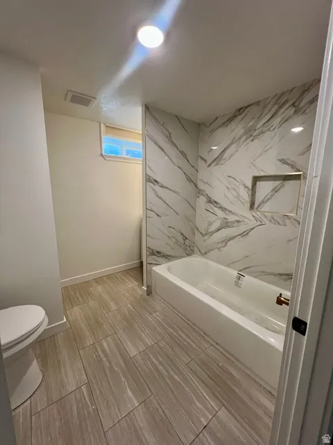 Bathroom featuring a white bathtub with a gold-toned faucet, surrounded by marbled tile walls