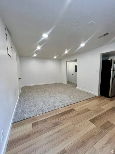 Open-concept living area featuring a neutral color palette, recessed lighting, and a combination of wood-finish flooring and grey carpet