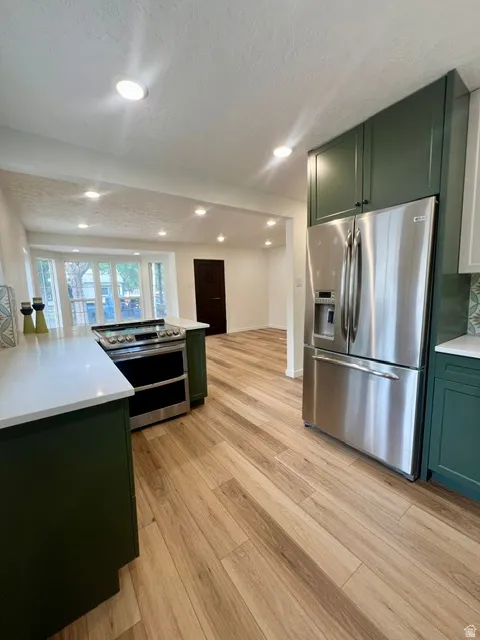 Kitchen featuring wood-finish flooring, stainless steel appliances, dark green cabinetry, white countertops, and recessed lighting