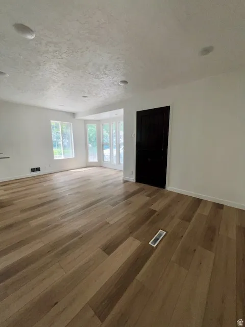 Spacious room featuring wood-finish flooring, white walls, and a textured white ceiling with recessed lighting